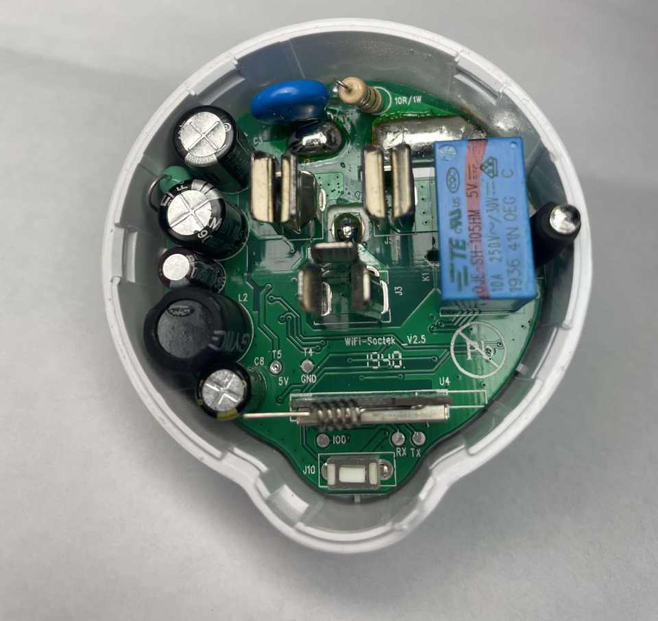 A top-down view of the Etekcity Voltson ESW01-USA-R6P's PCB. At the bottom of the PCB, there is an AI-Thinker ESP 01E module identifiable by its spring antenna. Below the ESP module, there are three test pads labeled, from left to right, as IO0, RX, and TX. Above and to the left of the ESP module, there are two test pads labeled, from left to right, as T5/5V and T4/GND.